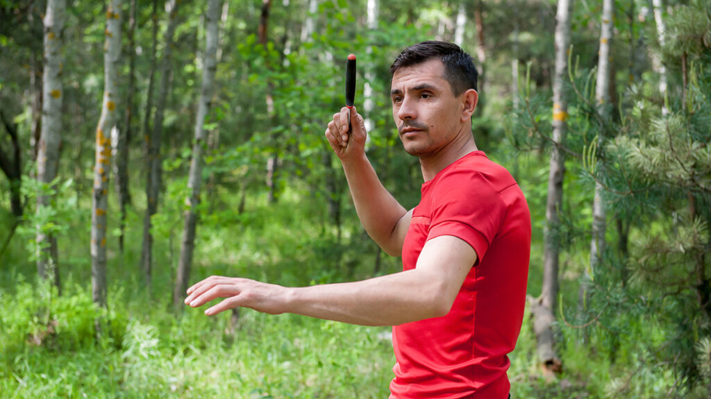 A man throws a knife at a target in the summer forest. Throwing a knife.